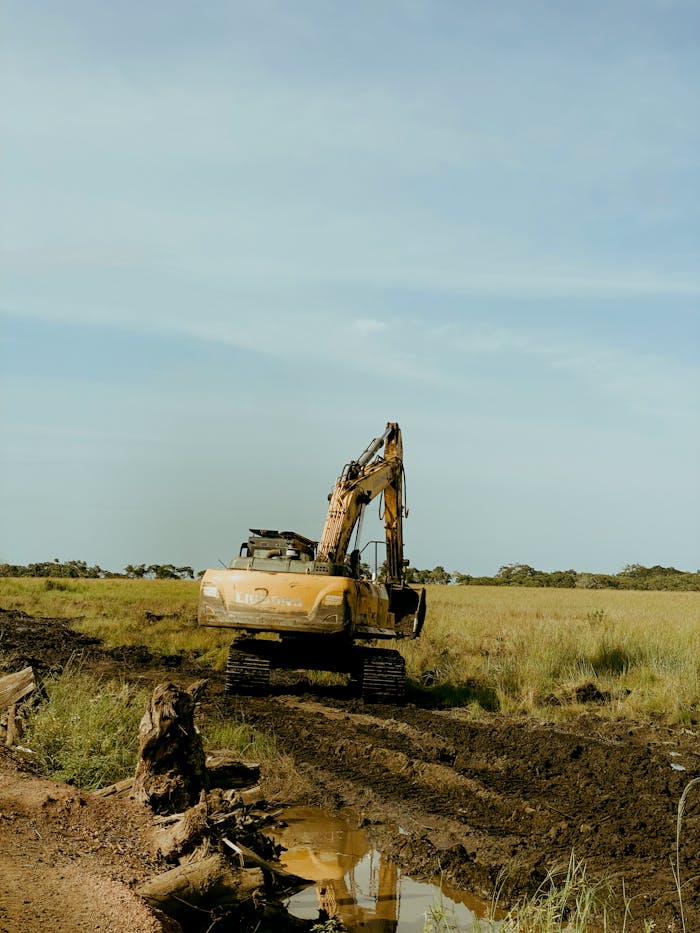 pexels-photo-36073761 An excavator at work on a rural construction site, surrounded by field and clear sky.